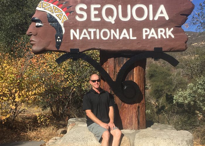 Steven sitting in front of Sequoia National Park sign